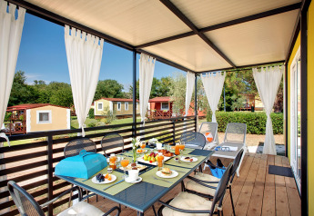 Overdekt terras bij Maravea Family Holiday Home met eettafel, witte gordijnen en uitzicht op chalets.