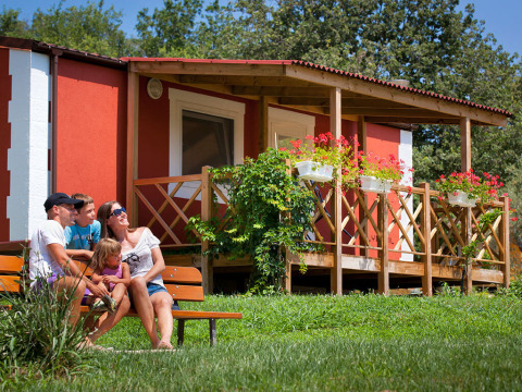 Een gezin zit op een bankje bij Maravea Premium Holiday Home, omringd door bloemen en een houten terras.