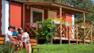 Una famiglia seduta su una panchina davanti a Maravea Premium Holiday Home con fiori e terrazza in legno.