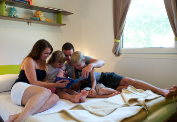 Famiglia che legge un libro insieme a letto nella Maravea Premium Holiday Home all'Aminess Planet Camping Maravea, Croazia.