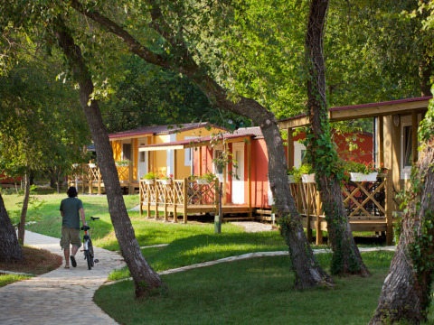 Man loopt met fiets langs kleurrijke Maravea Premium vakantiehuizen in een bosrijk resort in Kroatië.