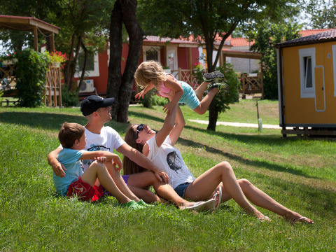 Een gezin ontspant en speelt op het gras voor hun Maravea Premium Holiday Home bij Aminess Planet Camping Maravea Resort in Kroatië.