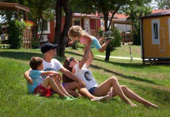 Una famiglia si rilassa e gioca sull’erba davanti alla Maravea Premium Holiday Home presso Aminess Planet Camping Maravea Resort in Croazia.
