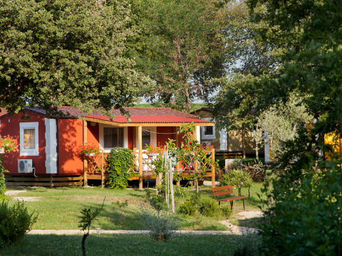 Rood vakantiehuisje met houten veranda te midden van groen bij Aminess Planet Camping Maravea in Kroatië.