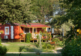 Casa vacanze rossa con veranda in legno tra alberi al Aminess Planet Camping Maravea Resort in Croazia.