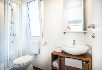 Bagno moderno e luminoso in una cabina con doccia, WC, lavabo, specchio e mobiletto con asciugamani.
