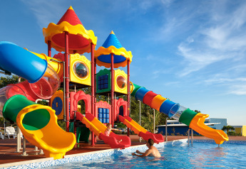 Scivoli colorati vicino a una piscina, con un bambino che gioca con un adulto sotto un cielo sereno.