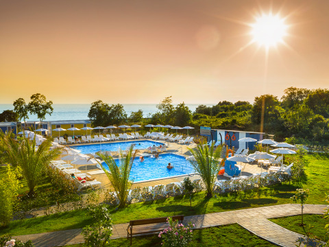 Piscina all'aperto presso una cabina con lettini, ombrelloni, palme e vista mare sotto il sole al tramonto.
