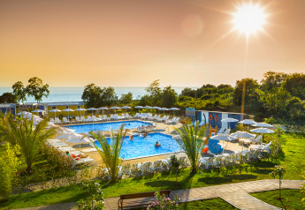 Piscina all'aperto presso una cabina con lettini, ombrelloni, palme e vista mare sotto il sole al tramonto.