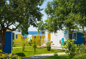 Cabina colorata vicino al mare tra alberi e prato verde, atmosfera rilassante per vacanze piacevoli.