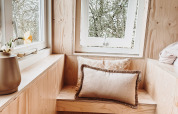 Gemütliche Sitzecke mit Holzbank, Kissen und Büchern am Fenster in Smûk Fjildhuske, Smûk Recreatie, Niederlande.