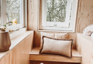 Acogedor rincón de ventana con banco de madera, cojines y libros en el lodge Smûk Fjildhuske, Smûk Recreatie, Países Bajos.