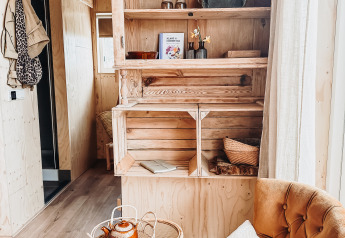 Cozy lodge corner with a comfy chair, tea table, and wood cabinet at Smûk Fjildhuske, Smûk Recreatie, Netherlands.