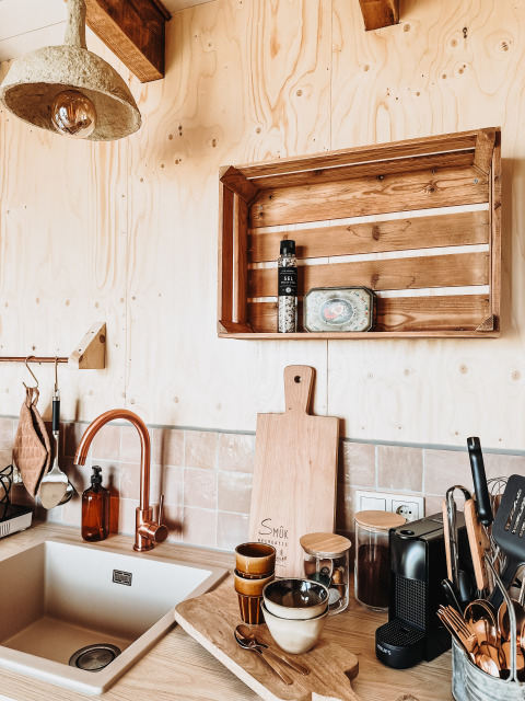 Moderne lodgekeuken met houten wandbekleding, koperen kraan en rustieke plank met keukengerei.