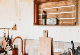 Moderne lodgekeuken met houten wandbekleding, koperen kraan en rustieke plank met keukengerei.