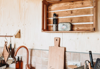 Cuisine moderne de lodge avec murs en bois, robinet en cuivre, étagère rustique et accessoires de cuisine.