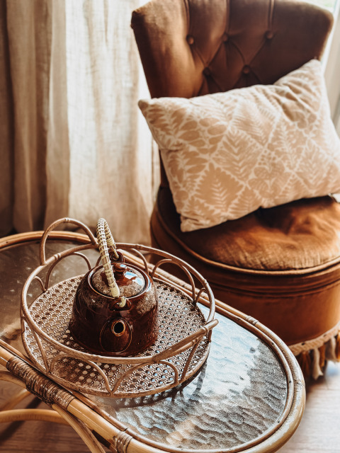 Silla marrón con cojín, tetera sobre bandeja de mimbre, mesa de cristal en Smûk Fjildhuske, Smûk Recreatie, Países Bajos.