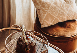 Silla marrón con cojín, tetera sobre bandeja de mimbre, mesa de cristal en Smûk Fjildhuske, Smûk Recreatie, Países Bajos.