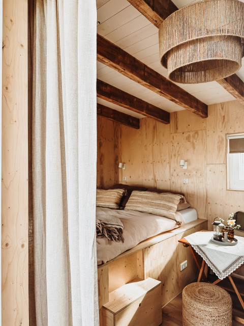 Knusse houten lodge slaapkamer met zichtbare balken, tweepersoonsbed en een klein gedekte tafeltje.