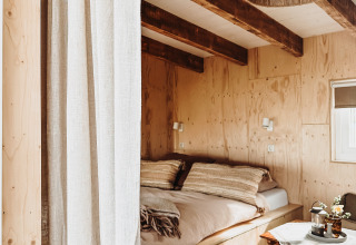 Dormitorio acogedor de madera con vigas vistas, cama doble, zona de estar y decoración natural.