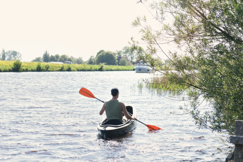 Man kajakt met oranje peddel op rivier bij Smûk Fjildhuske, Smûk Recreatie, Nederland, bomen op de oever.