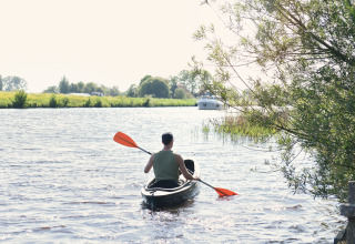 Man kajakt met oranje peddel op rivier bij Smûk Fjildhuske, Smûk Recreatie, Nederland, bomen op de oever.