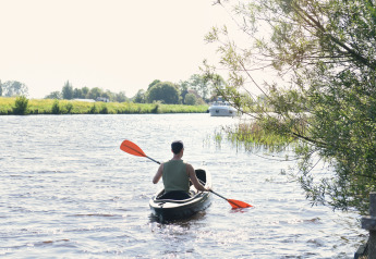 Man kayaking with orange paddle on river at Smûk Fjildhuske, Smûk Recreatie, Netherlands, trees nearby.