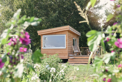 Una pequeña casa de madera llamada Smûk Tiny en Smûk Recreatie, Países Bajos, rodeada de flores.