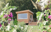 Kleines Holzhaus namens Smûk Tiny bei Smûk Recreatie in den Niederlanden, umgeben von Blumen.
