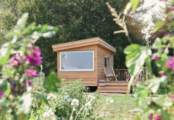 Klein houten huisje genaamd Smûk Tiny bij Smûk Recreatie in Nederland, omringd door bloemen.