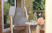 Gemütliche Terrasse am Smûk Tiny House in den Niederlanden mit Stuhl, Kissen, Blumen und Tisch.