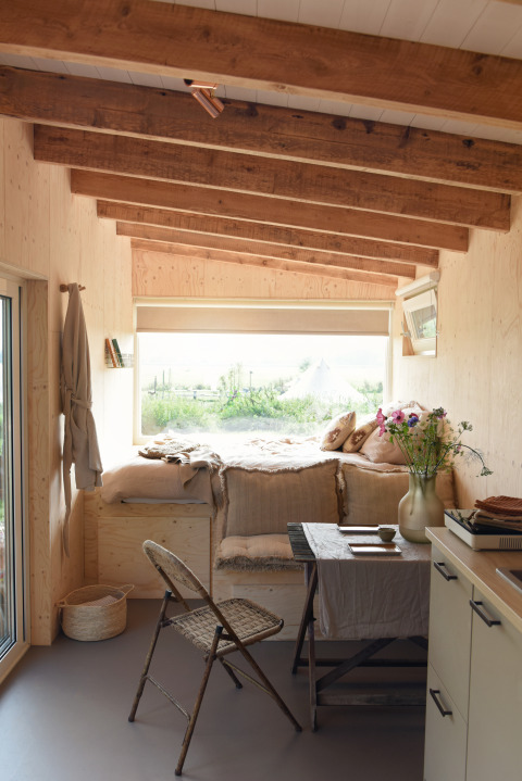 Interior acogedor de tiny house con vigas de madera, ventana grande y cama en Smûk Tiny, Países Bajos.
