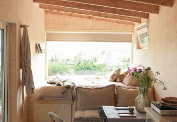Knappe tiny house met houten balken, groot raam en slaaphoek bij Smûk Tiny in Nederland.