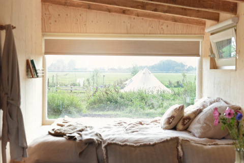 Vista desde la cama en una tiny house en Smûk Recreatie, Países Bajos, con un paisaje y tienda afuera.
