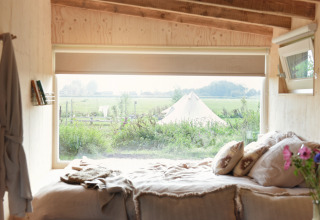 Vista desde la cama en una tiny house en Smûk Recreatie, Países Bajos, con un paisaje y tienda afuera.