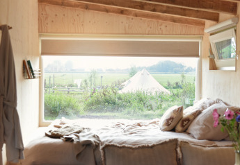 Uitzicht vanuit een tiny house bij Smûk Recreatie in Nederland, met een tent en weids uitzicht buiten.