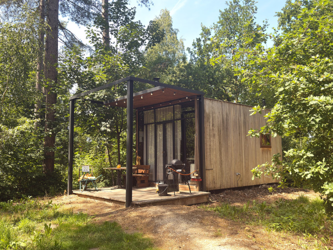 Pequeña cabaña de madera con porche y barbacoa en el bosque de Limburg, Bélgica, soleado.