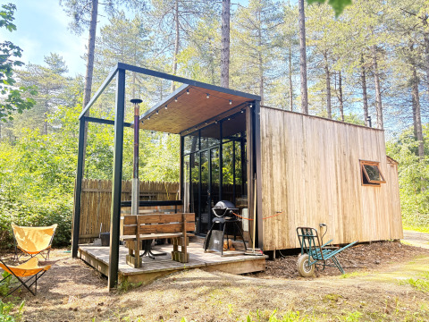 Kleine houten cabin met veranda, barbecue en zitbank bij Cosy Cabins in het bos van Limburg, België.