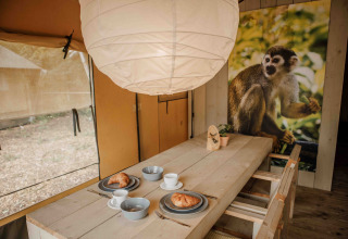 Indretning af en safaritelts spiseområde på Veluwepark de Bosgraaf med morgenmad og abe-plakat.