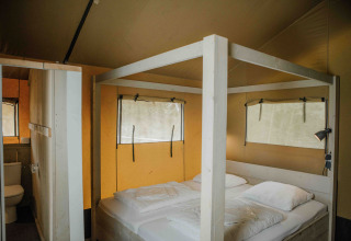 Vista interior de una tienda safari con cama doble y baño en Veluwepark de Bosgraaf, Países Bajos.
