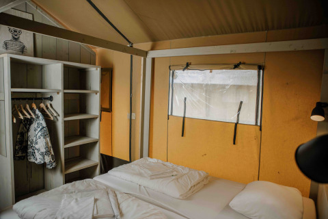 Indretning af soveværelse i safaritelt på Veluwepark de Bosgraaf i Holland, med seng og åben garderobe.