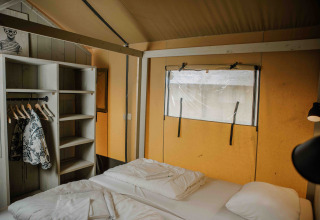 Indretning af soveværelse i safaritelt på Veluwepark de Bosgraaf i Holland, med seng og åben garderobe.