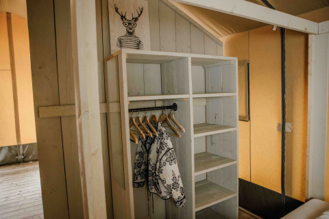 Holzkleiderschrank mit Kleiderbügeln und Jacken in einem Safarizelt im Veluwepark de Bosgraaf, Niederlande.