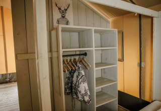Holzkleiderschrank mit Kleiderbügeln und Jacken in einem Safarizelt im Veluwepark de Bosgraaf, Niederlande.