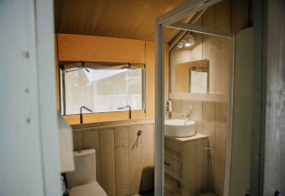 Baño de tienda safari con paredes de madera, lavabo y ventana en Veluwepark de Bosgraaf, Países Bajos.