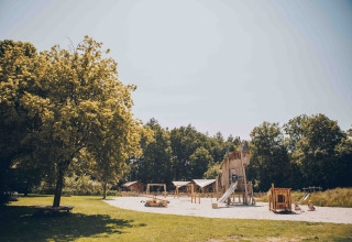 Spielplatz mit Holzspielgeräten und Rutsche am Safarizelt im Veluwepark de Bosgraaf, Niederlande, unter Bäumen.