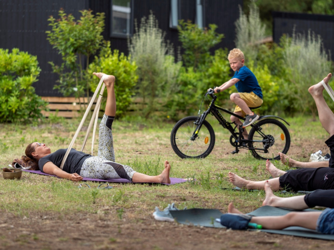 Buiten yogales op het gras bij Flower Camping Tamarins Plage, met een jongen op de fiets op de achtergrond.