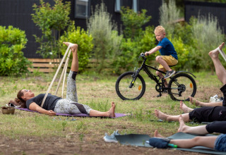 Buiten yogales op Flower Camping Tamarins Plage, met een jongen die op de achtergrond op de fiets rijdt.