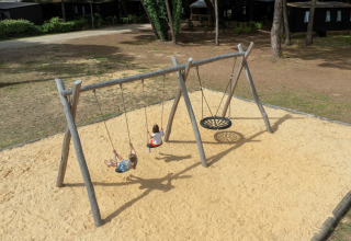 Bambini che giocano sulle altalene in un parco giochi sabbioso al Flower Camping Tamarins Plage, Nouvelle-Aquitaine, Francia.
