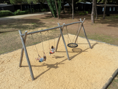 Children playing on swings in a sandy playground at Flower Camping Tamarins Plage, Nouvelle-Aquitaine, France.